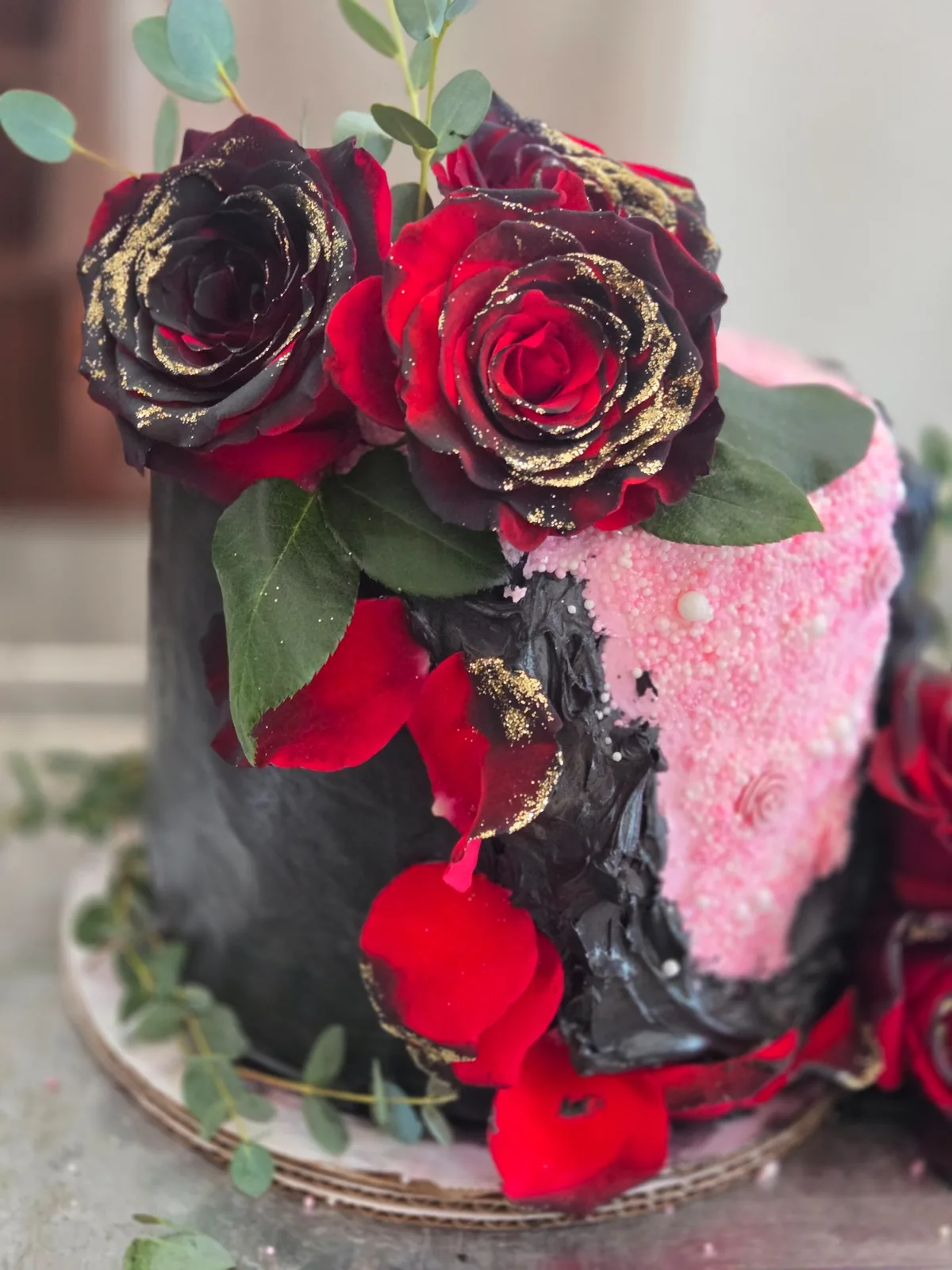 A black and pink custom celebration cake decorated with red roses and gold detail
